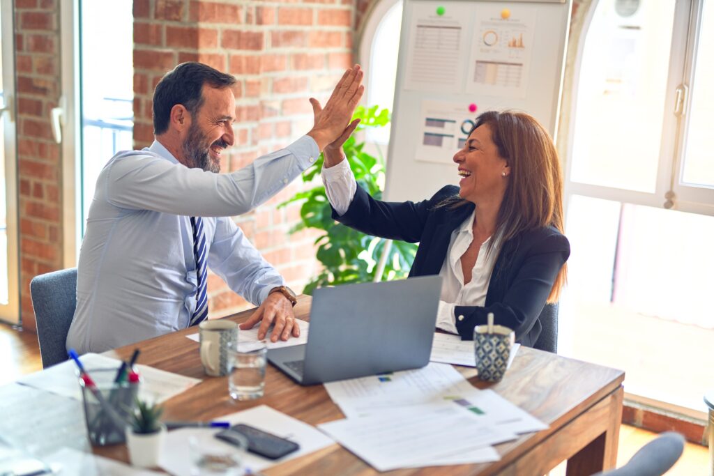 Two middle age business workers smiling happy and confident. Working together with smile on face hand giving high five at the office.