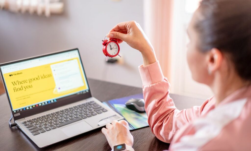 Woman sitting at laptop holding clock