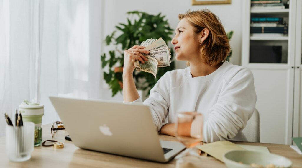 Woman in front of laptop holding wad of cash