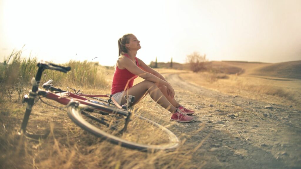 Woman at beach sitting beside bicycle getting physical self-care