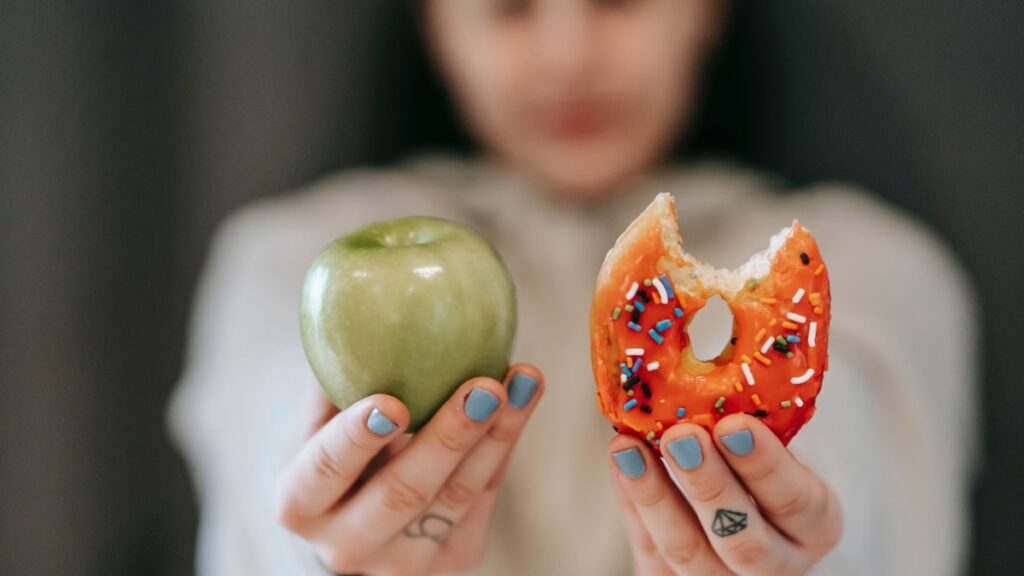 Woman holding apple and donut showing good versus bad habit